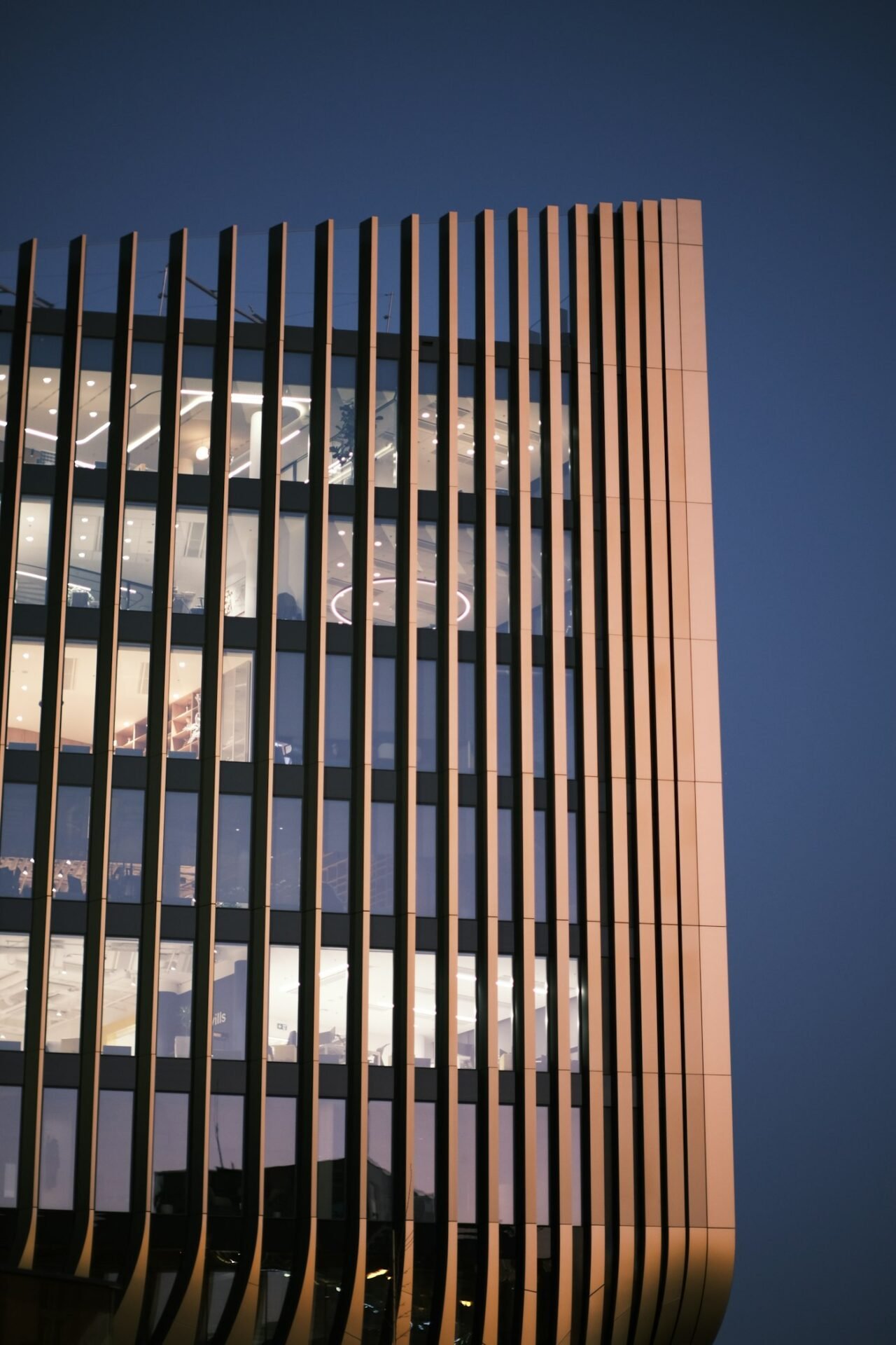 Modern high-rise building facade with vertical bronze fins, illuminated at dusk